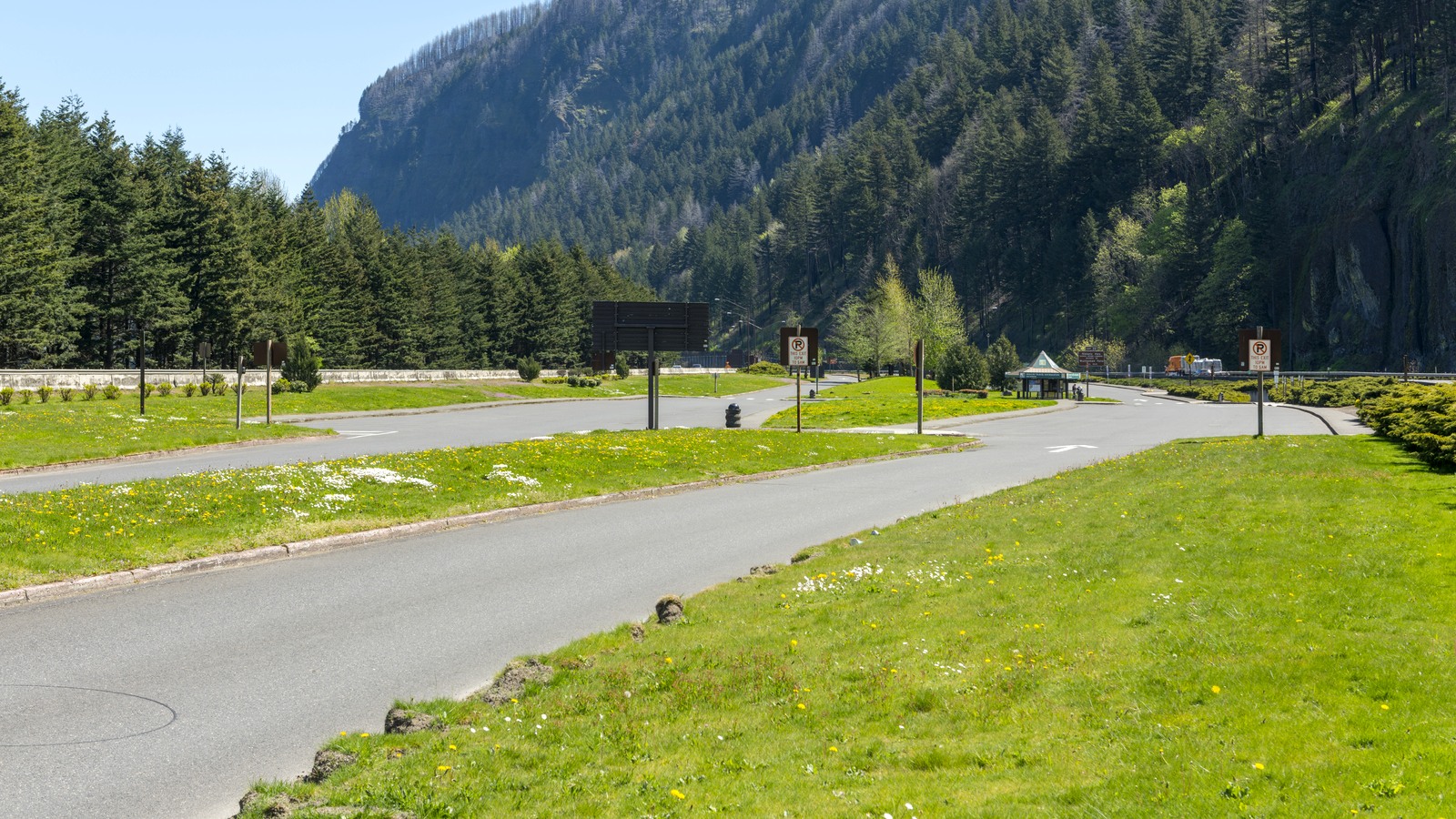 An empty paved parking area at Multnomah Falls beneath forested cliffs on a bright spring day.
